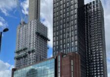 Tall modern skyscrapers under construction with cranes against a blue sky and scattered clouds