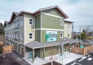 Three-story permanent modular construction building with green siding and large mural.