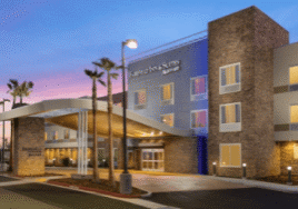 Evening view of a modern hotel with palm trees and a warmly lit entrance